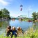 A busy amusement park with a roller coaster, a lake with a boating attraction and a person gliding overhead in a ski lift